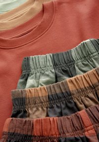 Bawełniany sweatshirt w kolorze rdzy z żeberkowym dekoltem, połączony z czterema parami luźnych szortów w odcieniach zieleni, brązu i szarości z elastycznymi pasami.