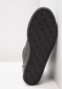 Black rubber sole with textured pattern featuring repeated logo. Side profile showing curved shape and smooth upper material.