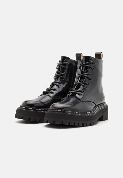 Schwarze Leder-Stiefeletten mit runden Zehen, Schnürdesign, dicken Gummisohlen und kontrastierendem weißen Nähen. Mit einer Zugschlaufe an der Ferse.