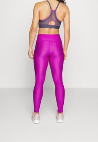 Top sportivo in tessuto grigio scuro con dettagli a taglio e accenti rosa, abbinato a leggings luminescenti, rosa brillante e scarpe da ginnastica chiare.