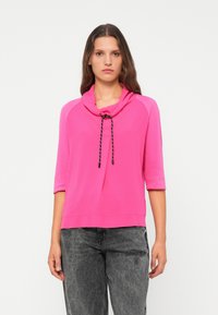Roze pullovertop met een kraag en een verstelbare trekkoord. Heeft driekwartmouwen en een relaxte pasvorm, gemaakt van zachte stof.