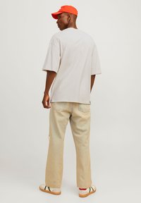 Lys grå oversized t-skjorte, beige høyt liv-jeans og kremfargede sneakers med grønne og røde detaljer. En lys orange caps fullfører antrekket.