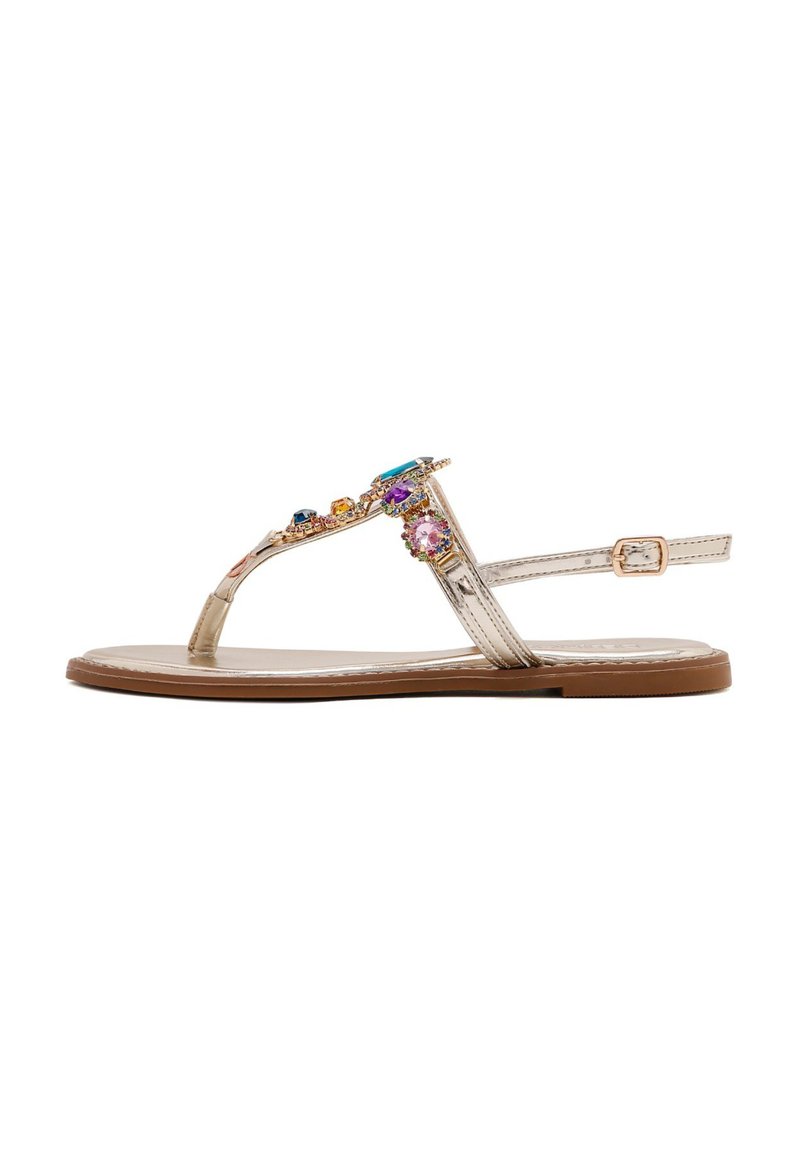 Las sandalias tipo thong metálicas doradas cuentan con una suela plana, una correa ajustable en el tobillo y adornos de gemas multicolores en la parte superior.