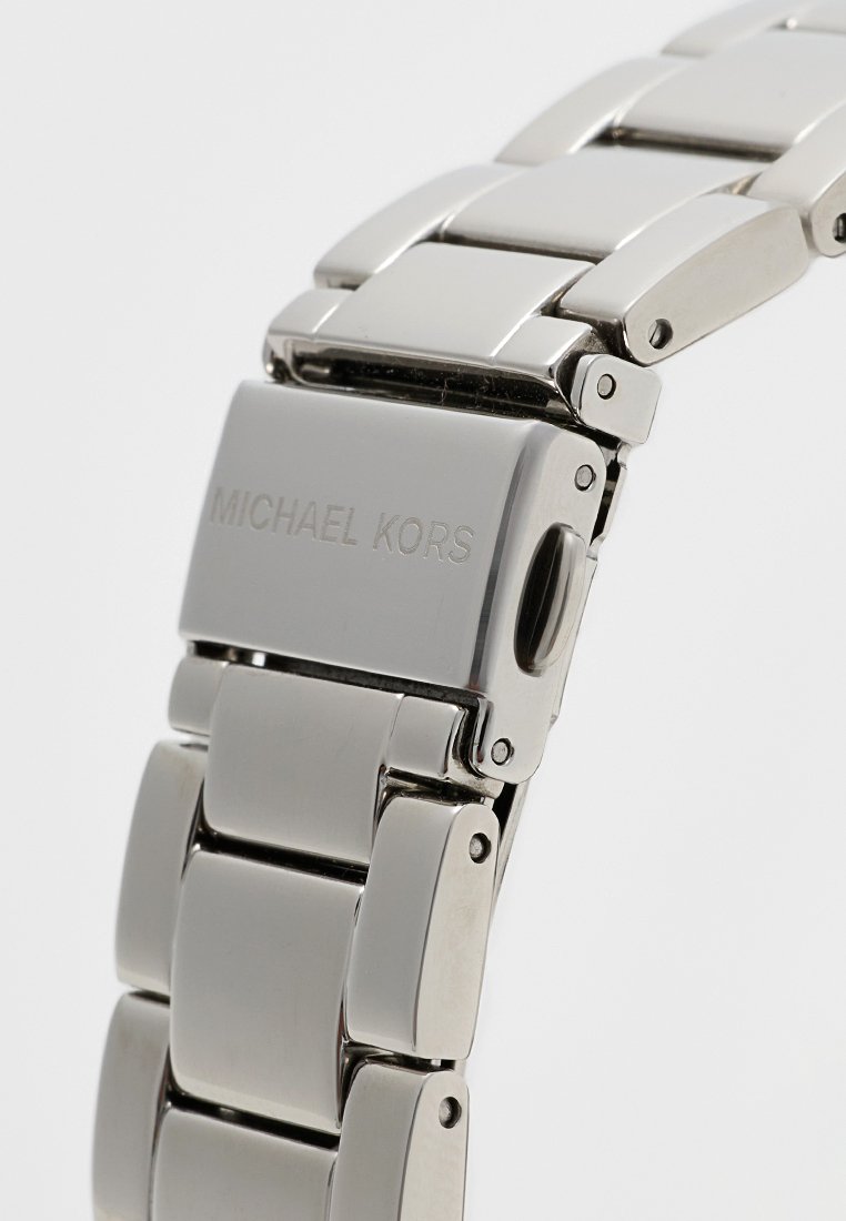 Bracelet de montre en acier inoxydable avec maillons rectangulaires et finition polie. Présente une gravure "MICHAEL KORS" sur le fermoir. Couleur argent.