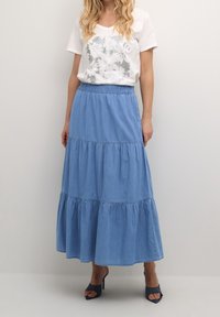 Ljusblå, flerlagrad jeanstyrka med elastisk midja, parad med en vit t-shirt med blommönster. Högklackade sandaler.