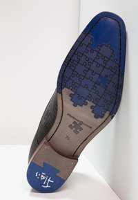 Chaussure en cuir noire avec un dessus texturé, dotée d'une semelle bleue à motif de puzzle et d'accents marron. Présentée avec la semelle vers le haut.