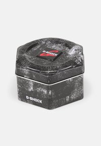 Black hexagonal tin with a textured surface, featuring a red and white G-SHOCK logo on the lid and minimalistic design accents.