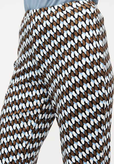 Κοντινή λήψη παντελονιού με διαγώνιο μοτίβο από καφέ, λευκά και ανοιχτόμπλε οβάλ σχήματα σε μαύρο φόντο.