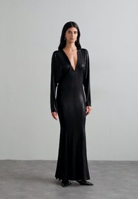Abito lungo nero con maniche lunghe, scollo a V profondo, silhouette aderente e orlo svasato, realizzato in un materiale liscio e lucido.