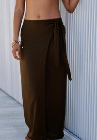 Jupe en tissu doux de couleur marron avec un lien à la taille, présentant une fente haute pour faciliter les mouvements. Texture lisse avec un design fluide.