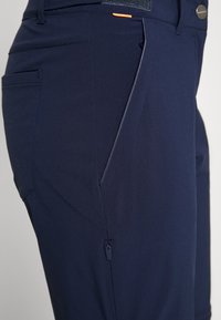 Pantalons bleu marine avec une texture lisse, dotés d'une poche zippée et d'une touche d'orange sur la ceinture. Design ajusté avec des coutures sur mesure.
