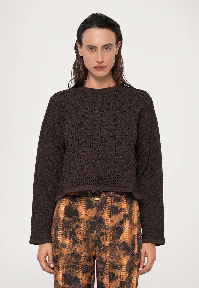 Maglione marrone a maglia con un motivo floreale testurizzato, scollo rotondo e maniche lunghe, abbinato a pantaloni con motivo arancione e nero.