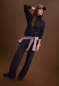 Maglione nero con collo alto, abbinato a pantaloni neri larghi. Un indumento lilla legato in vita, completato da un cappellino viola.