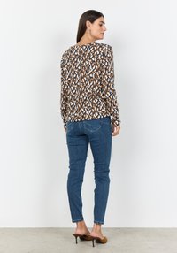 Langärmeliges Hemd mit einem abstrakten Muster in Braun, Marineblau und Creme; kombiniert mit enganliegenden blauen Jeans und braunen, absatzstarken Mules.