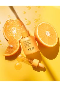 Upplysningsserum i en opak gul flaska med pipett, åtföljt av två apelsinhalvor och droppar på en gul yta.