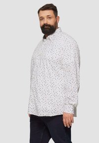 Witte overhemd met stippenpatroon in blauw, groen en beige. Met knopen, lange mouwen, ontspannen pasvorm. G gedragen met donkere jeans.