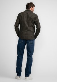 Zwarte, gemusterde lange mouwen shirt met een puntkraag, gecombineerd met blauwe spijkerbroek en witte sneakers, met een relaxte pasvorm en casual stijl.