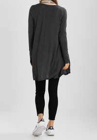 Túnica larga de color gris oscuro hecha de tela suave, con escote redondo y aberturas laterales, combinada con leggings negros y zapatillas blancas.