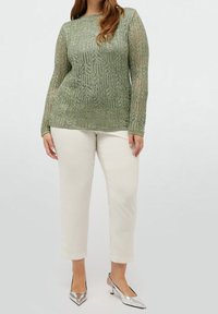 Pull en maille à motifs verts avec une finition texturée, manches longues et col rond, associé à un pantalon beige clair ajusté et des talons argentés.