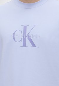 Ανοιχτό μωβ πουκάμισο με μεγάλο «cK» και «Calvin Klein» κεντημένα με νήμα σε ταιριαστή μωβ απόχρωση στο στήθος.