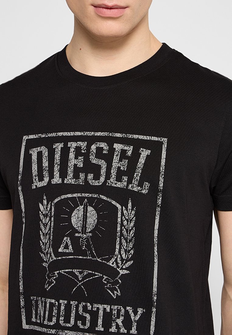 T-shirt en coton noir présentant un imprimé graphique gris usé avec "DIESEL" et "INDUSTRY", entouré de détails en laurier et en emblème.