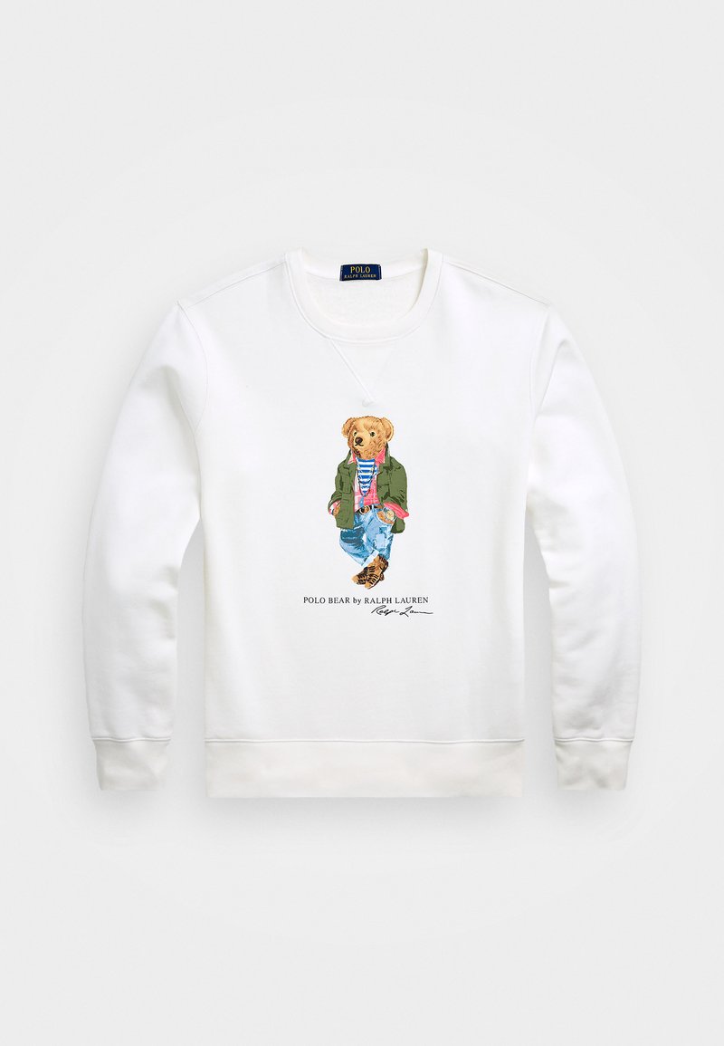 Λευκό φούτερ με κεντημένη αρκούδα που φορά πράσινο μπουφάν και μπλε τζιν, με ριγωτό πουκάμισο και καφέ παπούτσια.