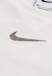 Hvidt, tekstureret stof med et netdesign; har en flerfarvet broderet Nike swoosh-logo og en V-formet halsudskæring.