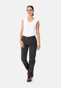 Lätt vit ärmlös topp med V-ringning, matchad med mörkgrå byxor med avslappnad passform och justerbar nederkant. Bruna vandringskängor.