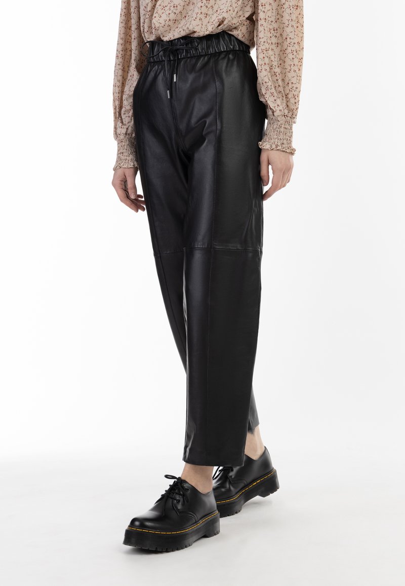 Zwarte neplederen broek met een elastische tailleband, met een taps toelopend ontwerp en een gladde textuur, gecombineerd met chunky zwarte schoenen.