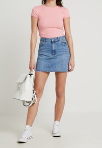 Růžový pruhovaný top s krátkým rukávem, denimová mini sukně s roztrhaným lemem, bílý batoh a bílé tenisky. Neformální outfity s jednoduchými designovými prvky.
