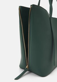 Grøn lædertaske med guldlynlås og matchende beslag. Ydersiden har en glat tekstur og et struktureret design.