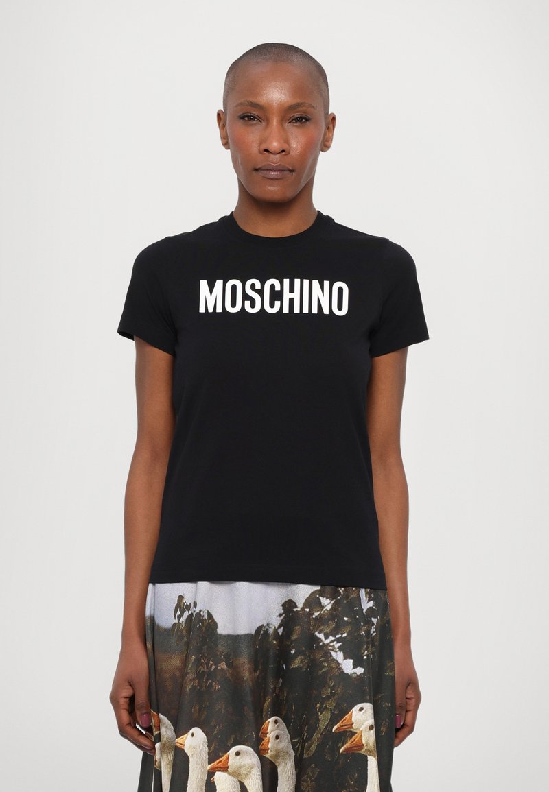 Melna kokvilnas T-kreklu ar uzrakstu "MOSCHINO" treknā baltā burtu stilā krūtīs, apvienots ar druku svārkiem, kuros attēloti zīļi.