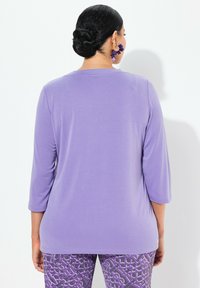 Lilafarbene Langarmbluse mit rundem Halsausschnitt, kombiniert mit lila gemusterten Leggings. Die Bluse hat eine glatte Textur und eine figurschmeichelnde Passform.