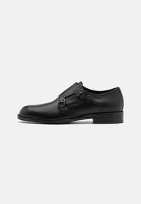 Black leather dress shoe with dual buckles, sleek silhouette, and round toe. Features a low heel and smooth texture.