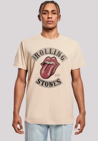 Beige katoenen t-shirt met een grote versleten graphic van het logo van de Rolling Stones, met een rode tong en zwarte tekst. Standaard pasvorm.