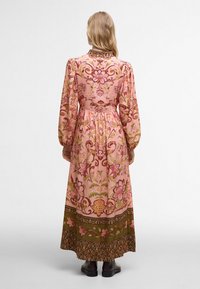 Robe maxi en tissu rose ornée de motifs floraux, avec de longues manches bouffantes, une taille ajustée et un ourlet à motifs verts contrastants.