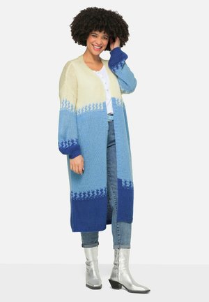 Lange gebreide cardigan met een verloop van crème naar lichtblauw naar donkerblauw. Comfortabele textuur met decoratieve sterpatronen op de mouwen.