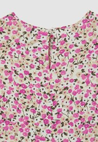 Top floreale con sfondo crema, fiori rosa e bianchi, maniche corte e chiusura a bottone sul retro con aperture a forma di chiave.