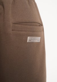 Brune bomuldsjoggers med en sidelomme og et lille logo-patch. Den glatte tekstur og den tapered design giver en afslappet pasform.