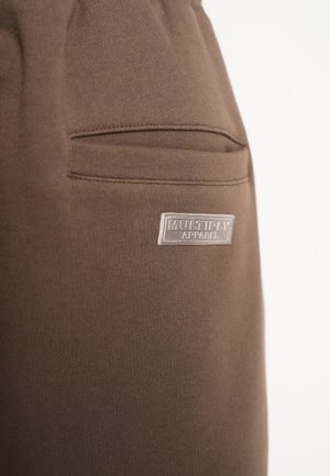 Brown cotton joggers with a side pocket and a small logo patch. Smooth texture and tapered design provide a relaxed fit.