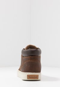 Bruine leren hoge sneakers met een bruin gewatteerd kraagje, witte rubberen zool en het Timberland-logo in reliëf op de hiel.