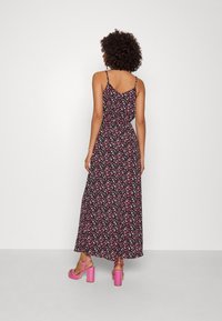 Robe maxi avec des bretelles fines, en tissu noir ornée d'un motif floral en rose et blanc. Portée avec des sandales à talons bloc roses.