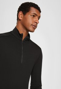 Fekete negyedzippes pulóver hosszú ujjakkal, puha anyagból készült, magas gallérral és letisztult dizájnnal, minimális varrási részletekkel.