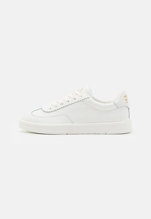 White sneakers with a smooth leather surface, subtle tonal stitching, round laces, and a textured rubber sole. Gold branding at the heel.