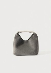 Sac à main en daim gris avec une poignée courbée en argent, forme souple et structurée, au design minimaliste sur un fond clair uni.