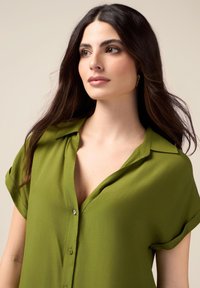 Groene blouse met korte mouwen, een ontspannen pasvorm, kraag en knoopsluiting. De stof lijkt lichtgewicht en soepel met een subtiele glans.