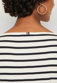 Pasiasty top w czarno-białe poziome paski, z szerokim dekoltem i małym akcentem w kolorach czerwonym, białym i niebieskim na tylnym kołnierzu.