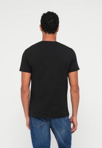 Μαύρο κοντομάνικο μπλουζάκι με στρογγυλή λαιμόκοψη, φτιαγμένο από μαλακό ύφασμα. Διαθέτει απλό σχέδιο, χωρίς μοτίβα ή διακοσμητικά στοιχεία, φορεμένο με μπλε τζιν.