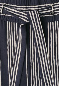 Navy blue fabric with vertical white stripes and tied drawstring threaded through metal eyelets at the waistband.