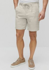 Beige- värinen pellavashortsit, joissa on naru vyötäröllä, kaksi sivutaskua ja rento istuvuus, yhdistettynä vaaleanruskeisiin mokkasneakereihin.